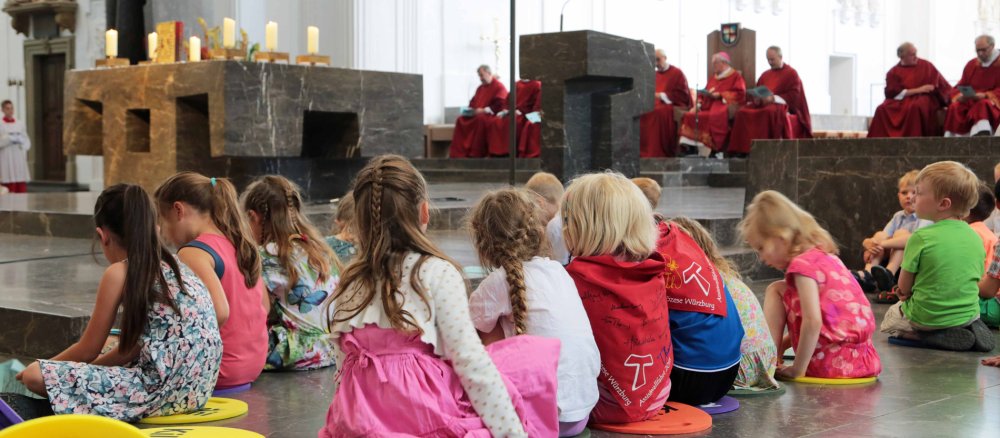 Kindergartenkinder sitzen während einer Messe im Würzburger Dom auf dem Boden im Altarraum.