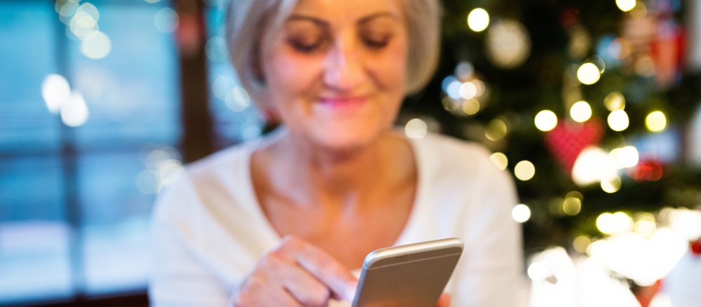 Eine Frau tippt einen Text in ihr Smartphone, im Hintergrund der Weihnachtsbaum.