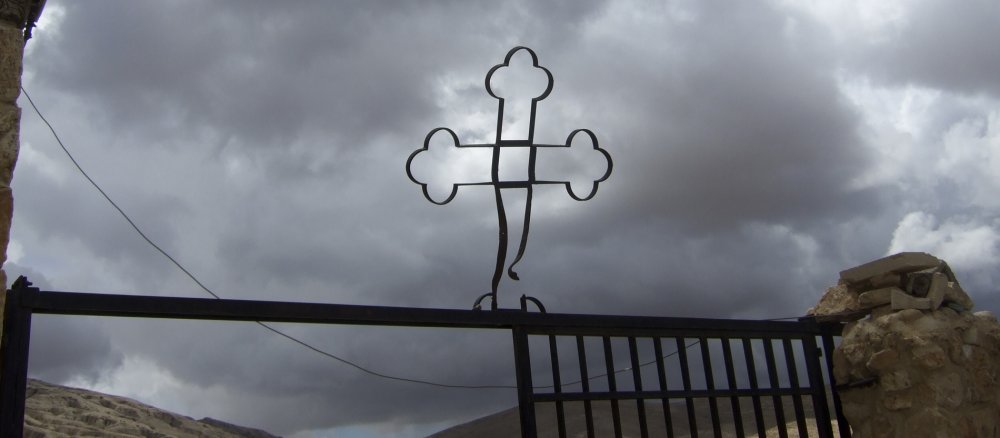 Ein verbogenes Kreuz auf einem Zaun vor düsterem bewölktem Himmel