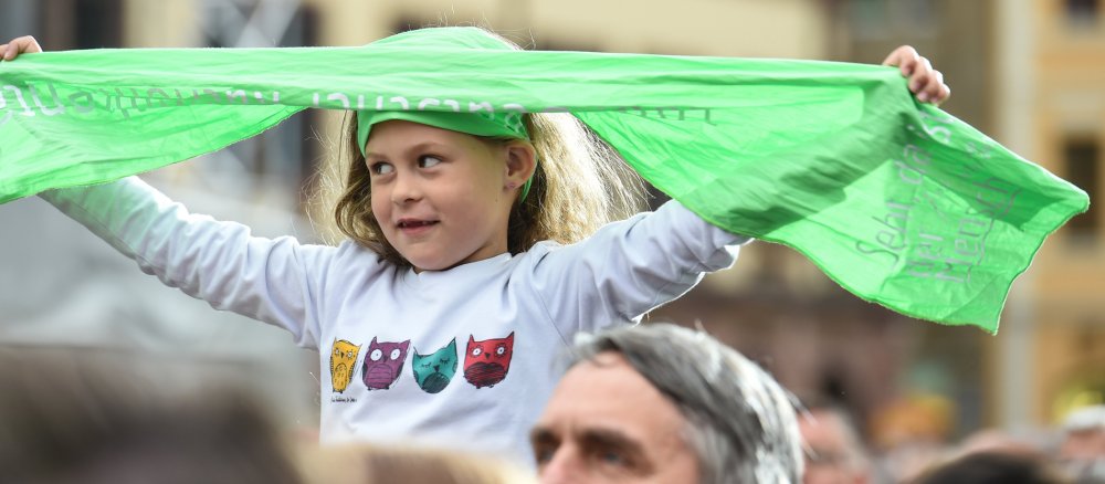 Ein Mädchen hält den grünen Schal des Katholikentags hoch. Zu lesen ist das Motto des Katholikentags "Seht, da ist der Mensch".