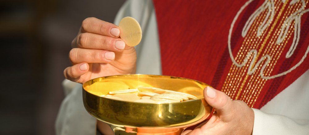 A woman in liturgical vestments holds up a host