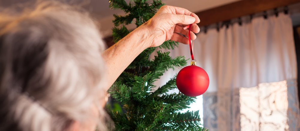 Eine alte Frau schmückt einen Weihnachtsbaum mit einer roten Glaskugel.