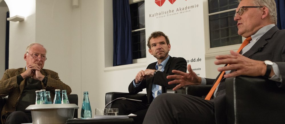 Drei Menschen sitzen an einem Tisch und diskutieren miteinander.