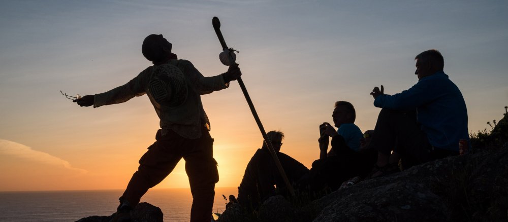 Eine Gruppe Pilger steht und sitzt auf einem Felsen am Meer.