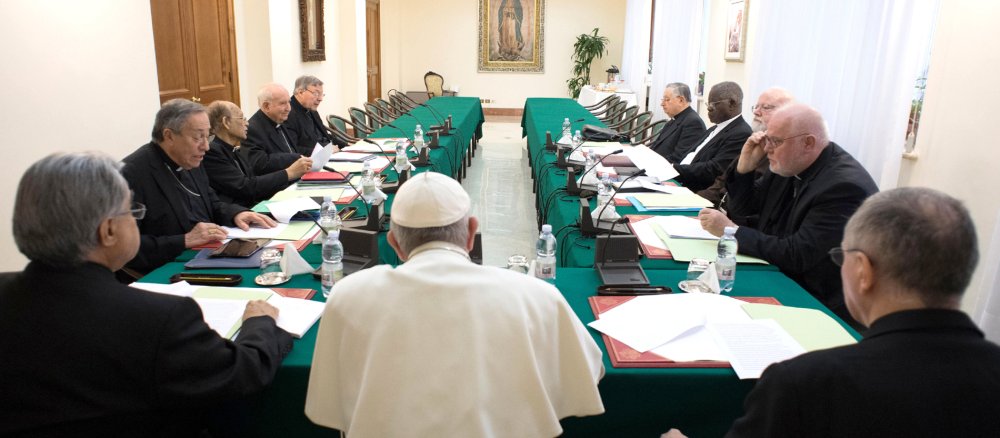 Papst Franziskus sitzt mit Kardinälen aus dem Kardinalsrat an einem Konferenztisch zusammen.