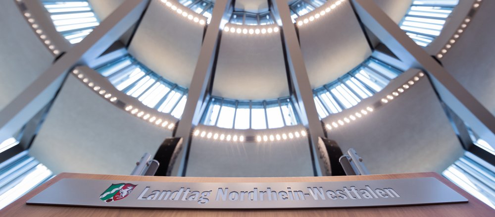 "Landtag Nordrhein-Westfalen" steht am Rednerpult im Plenum des Landtags unter der Kuppel.