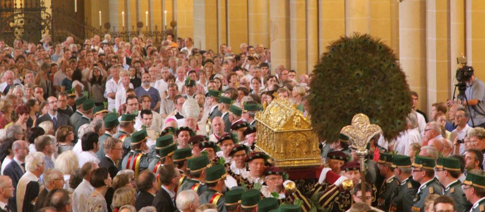 Ein goldener Schrein wird durch eine vollbesetzte Kirche getragen.