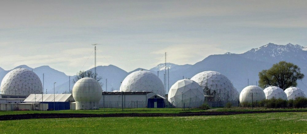Zwischen einer Bergwiese und den Alpen stehen kugelförmige Gebäude.