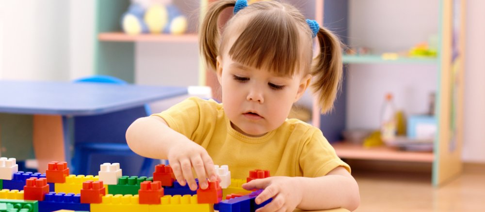 Kleines Mädchen mit Zöpfchen spielt mit Lego im Kindergarten