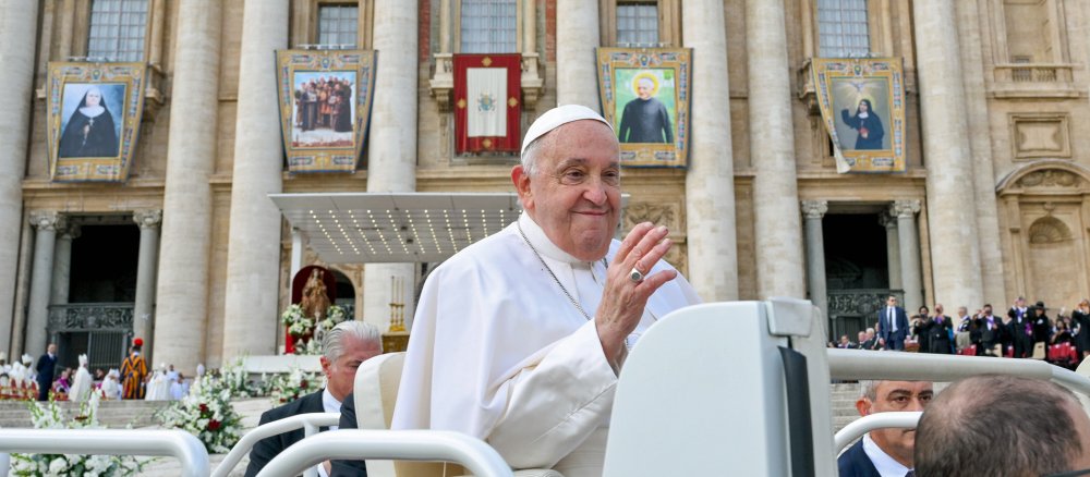 Papst Franziskus fährt mit dem Papamobil, im Hintergrund Banner von Heiilgen