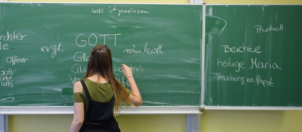Eine Schülerin steht im Religionsunterricht an der Tafel.