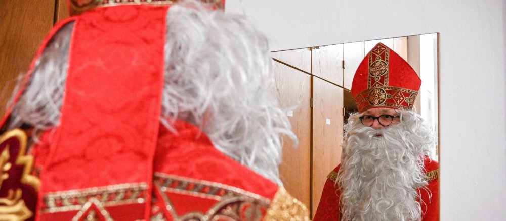 A man in a St Nicholas costume looks at himself in the mirror