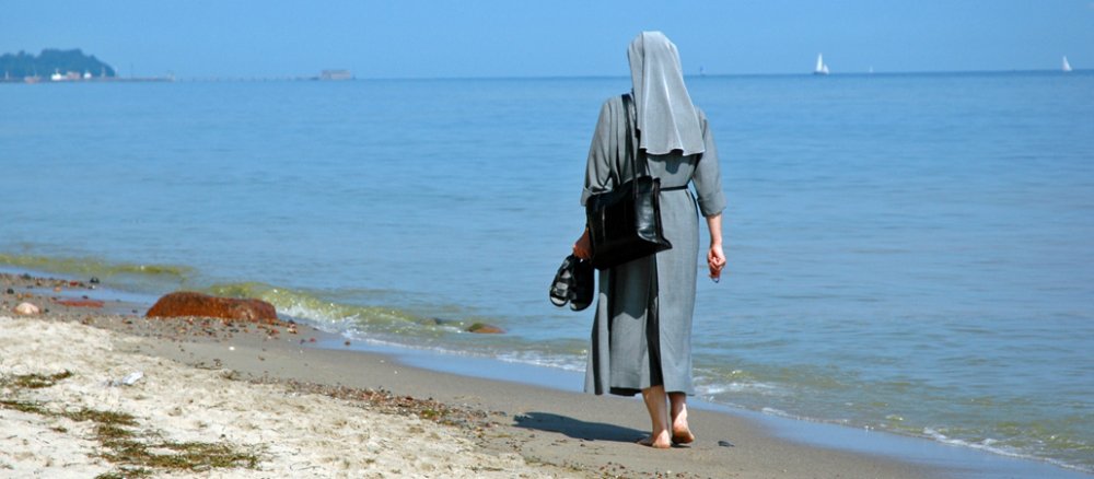 Eine Nonne läuft barfuß am Strand entlang.