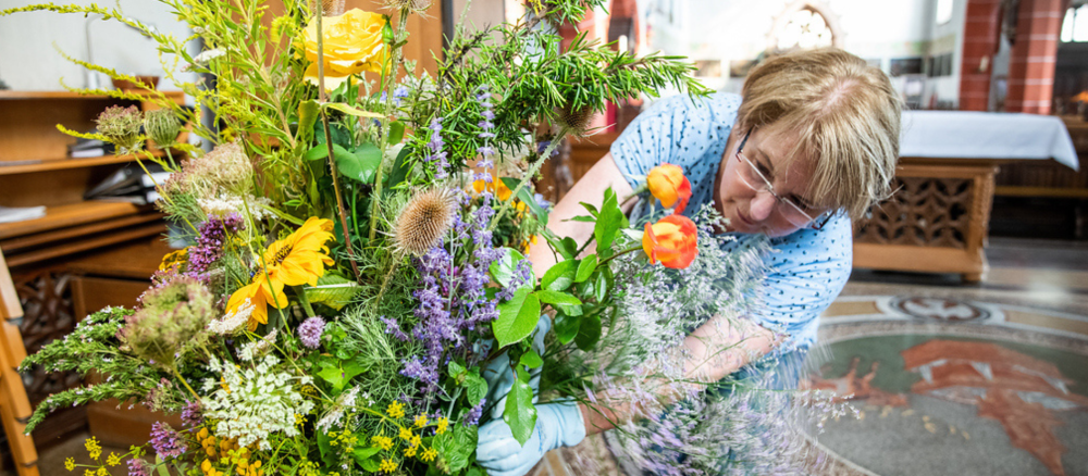 Eine Frau zupft einen großen Blumenstrauß zurecht aus gesammelten Kräutern und Wiesenblumen für einen Gottesdienst anlässlich von Mariä Himmelfahrt am 14. August 2021 in der Kräuterkirche in Bingen.