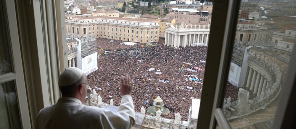 Papst Franziskus vor offenem Fenster und einer Menschenmenge.