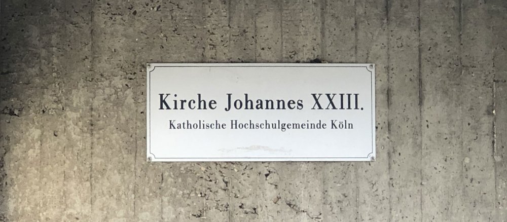 Schild der KHG Köln an der Kirche St. Johannes XXIII.