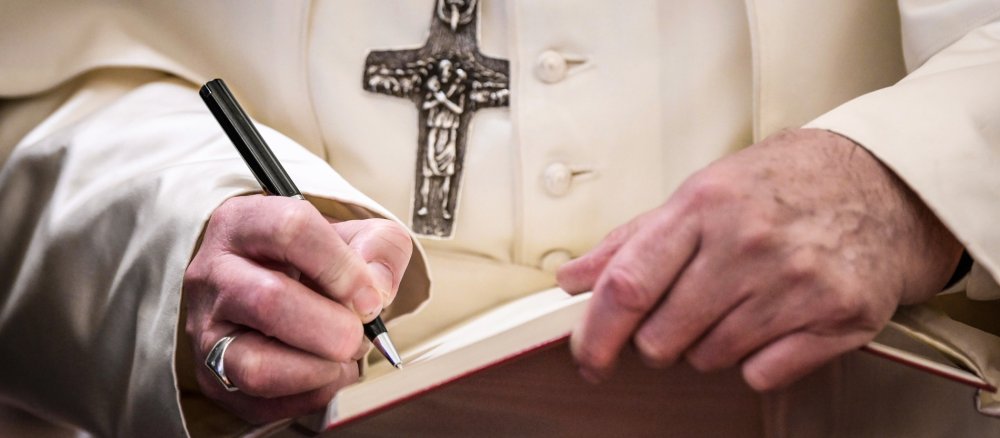 Papst Franziskus schreibt mit einem Kugelschreiber in ein Heft