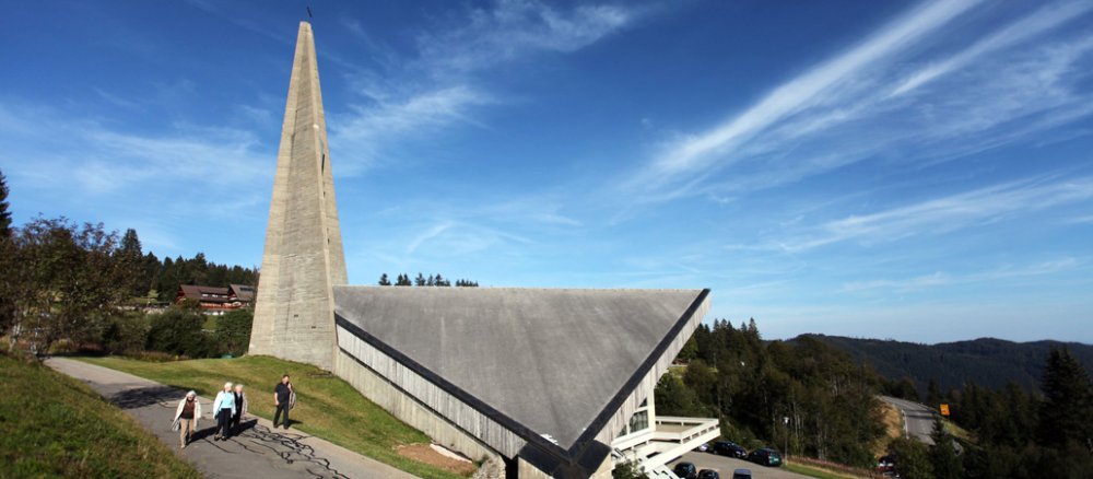 Eine Kirche mit modernem Spitzdach steht auf dem Feldberg - beäugt von ein paar Wanderern.