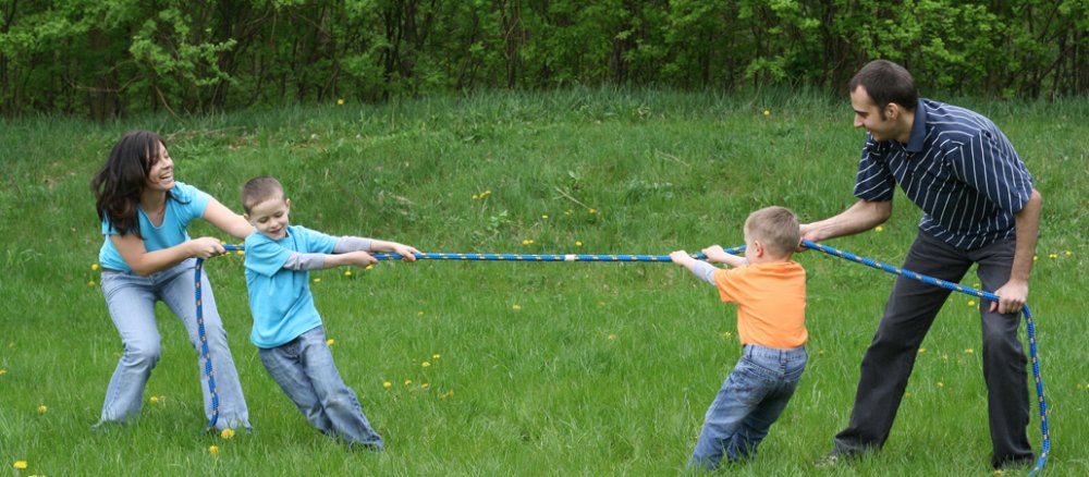 Eine junge Familie spielt Tauziehen auf einer Wiese.