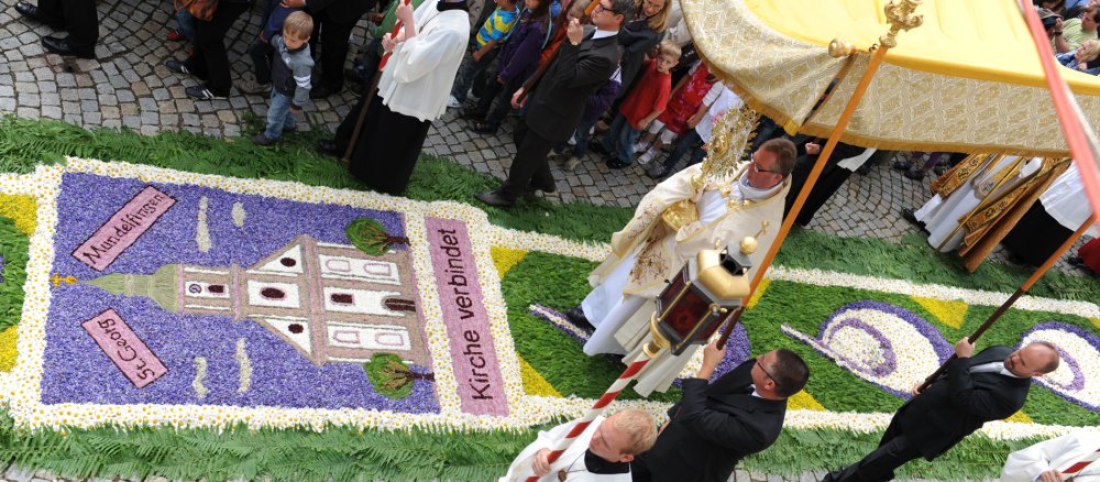 Ein Priester läuft während der Fornleichnamsprozession mit der Monstranz über einem Blumenteppich.
