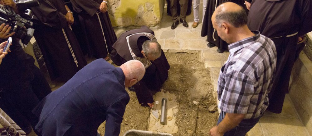 Mehrere Männer stehen um ein Loch im Boden, in das ein Stein versenkt wurde