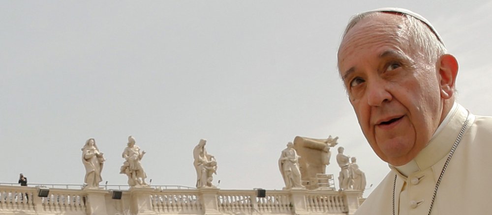 Papst Franziskus schmunzelt, im Hintergrund die Firguren auf den Kolonnaden.