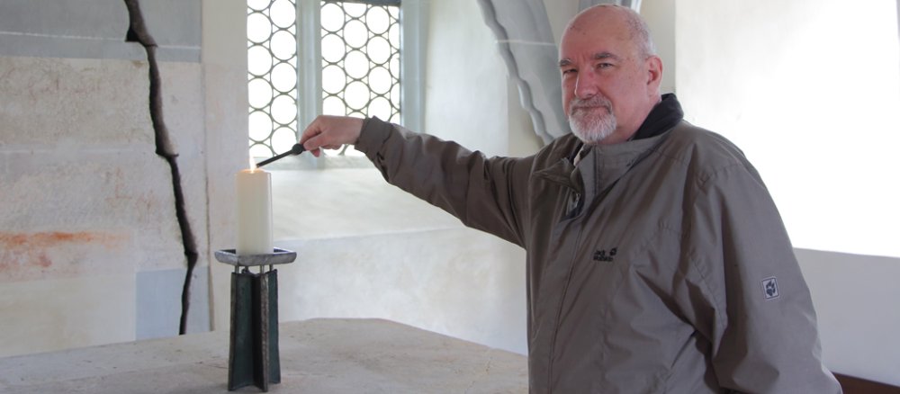 Ein brätiger Mann steh in einer hellen Kapelle und zündet eine Kerze an.