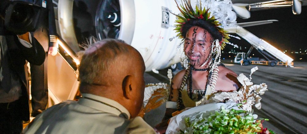 Papst Franziskus wird bei seiner Ankunft auf dem Flughafen von Port Moresby von einer Person in traditioneller Kleidung mit Blumen empfangen