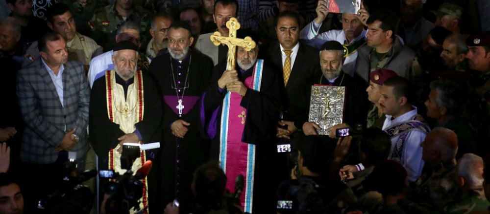 Ein Priester hält inmmitten einer Menschenmenge ein Kreuz.