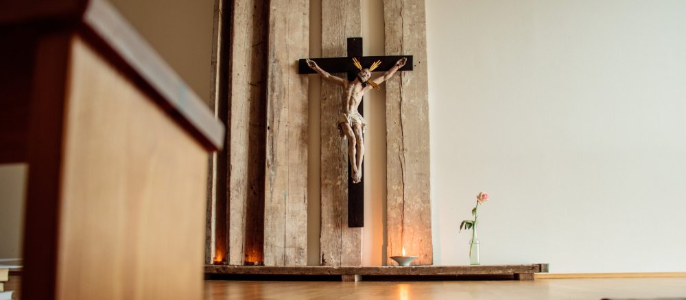 Im Vordergrund steht ein Gebetshocker, im Hintergrund ist ein Kreuz mit Corpus zu sehen.