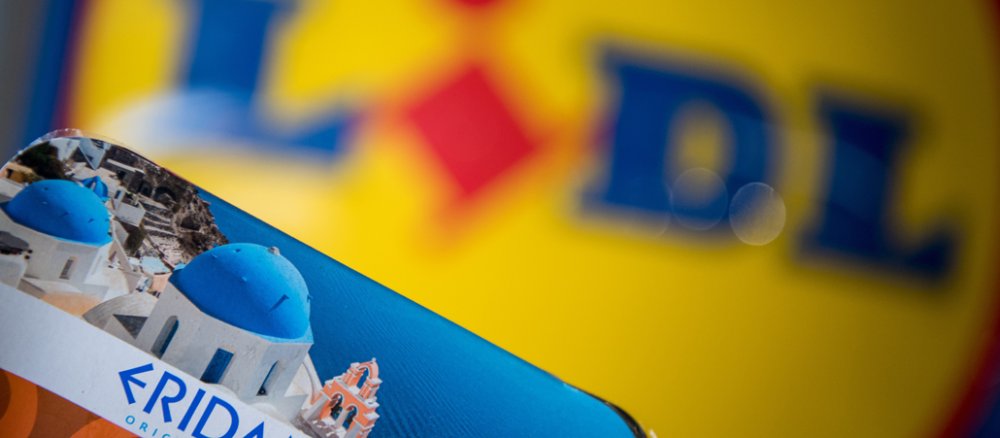 Eine Packung mit Moussaka der Lidl-Eigenmarke Eridanous liegt vor einem Lidl-Schild.
