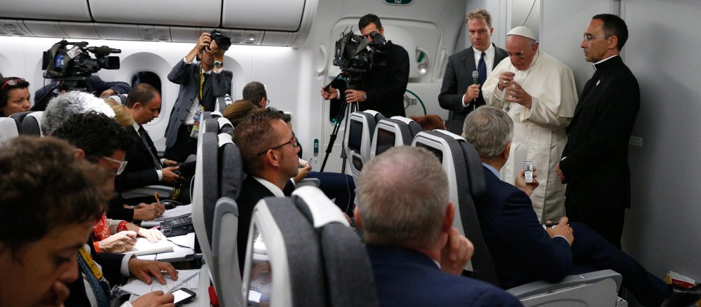 Franziskus steht im Flugzeug und spricht mit Passagieren.