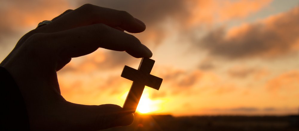 Eine Hand hält ein Kreuz vor dem Sonnenuntergang