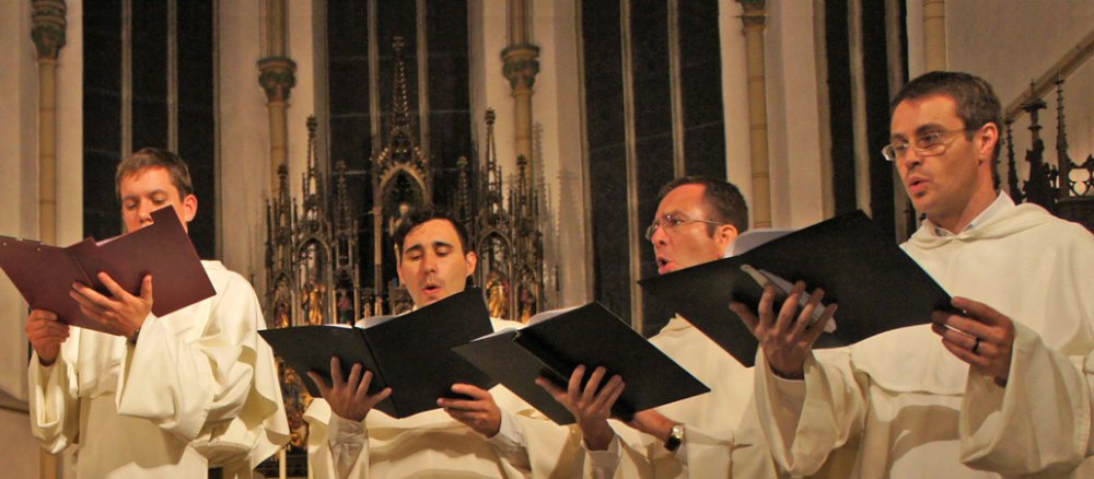 Sechs Mönche stehen im Halbrund in einer Kirche und singen.