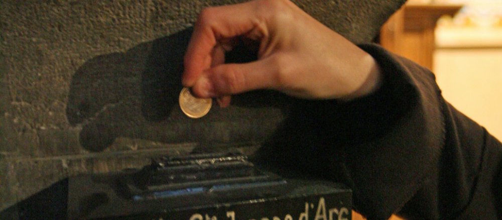 Ein Mensch wirf Geld in einen Opferstock.
