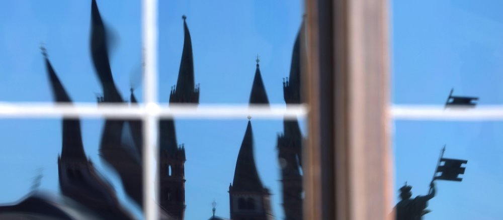 Die Türme des Würzburger Doms spiegeln sich verzerrt in einem Fenster der Residenz.