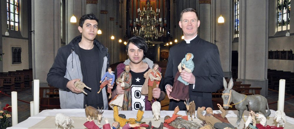 Zwei junge Flüchtlinge und ein Priester präsentieren in einer Kirche Krippenfiguren, die gestohlen waren.