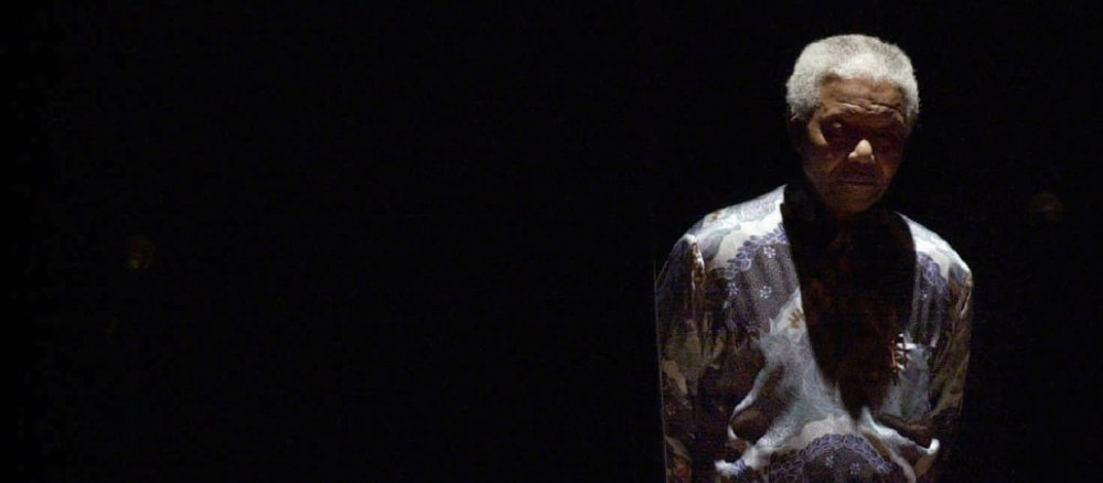 Nelson Mandela im Rampenlicht einer Bühne vor schwarzem Hintergrund.