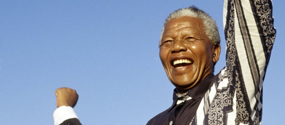 Nelson Mandela im Rampenlicht einer Bühne vor schwarzem Hintergrund.