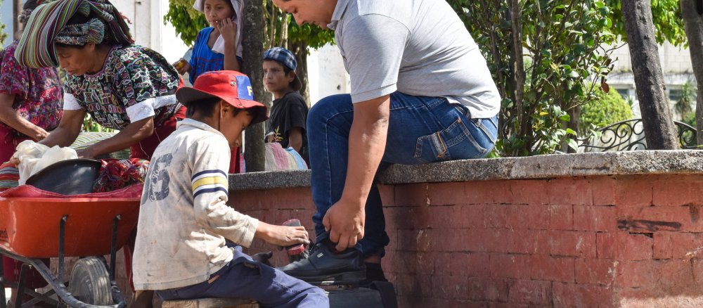 Ein Junge putzt in Guatemala die Schuhe eines Mannes.