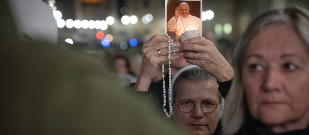 Eine Ordensschwester hält einen Rosenkranz, eine Kerze und ein Bild von Papst Franziskus
