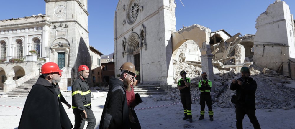 Benediktinermönche mit Schutzhelmen vor der eingestürzten Basilika St. Benedikt in Norcia, Mittelitalien.