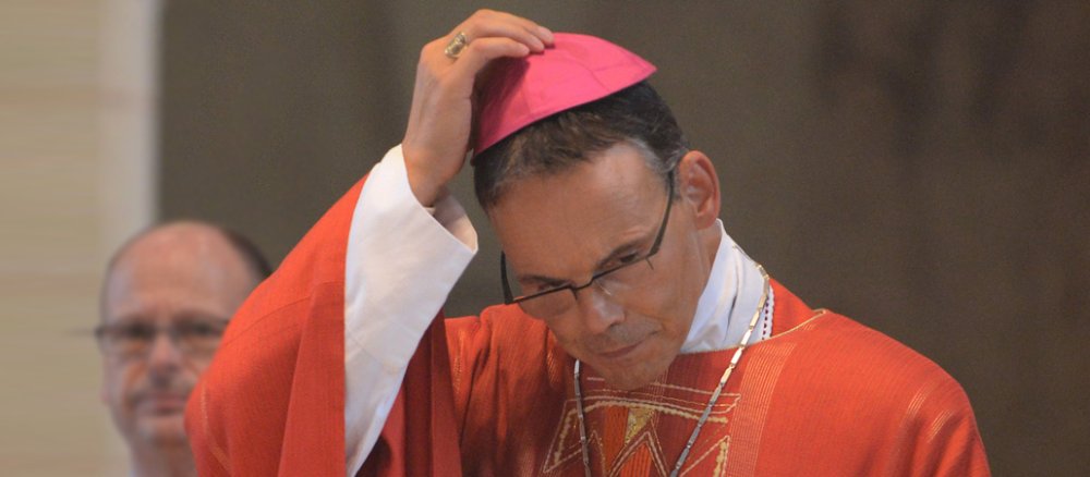 Bischof schaut am Altar nach unten und zieht seine Bischofsmütze.