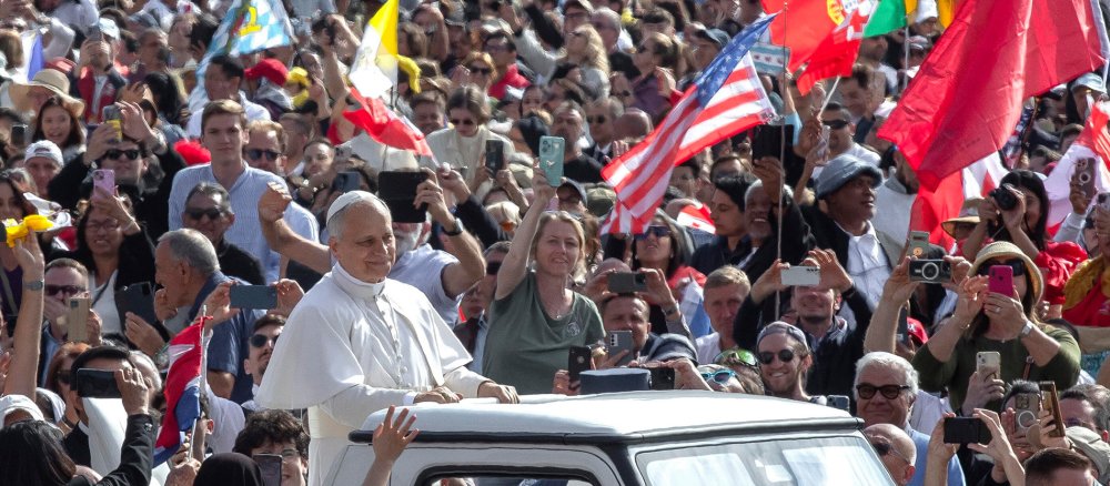 Papst Leo XIV. im offenen Papamobil auf dem Petersplatz inmitten einer Menschenmenge mit Flaggen.