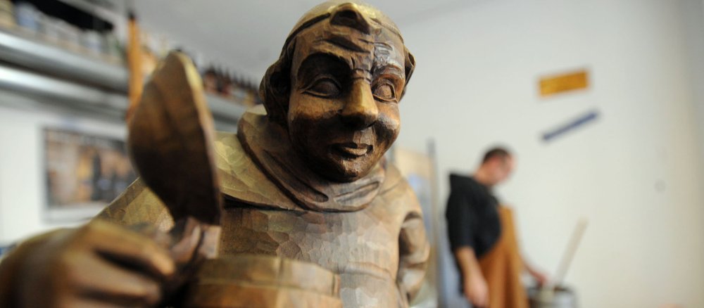 hölzerne Mönchsfigur mit Bierkrug im Hintergrund Mönch beim brauen