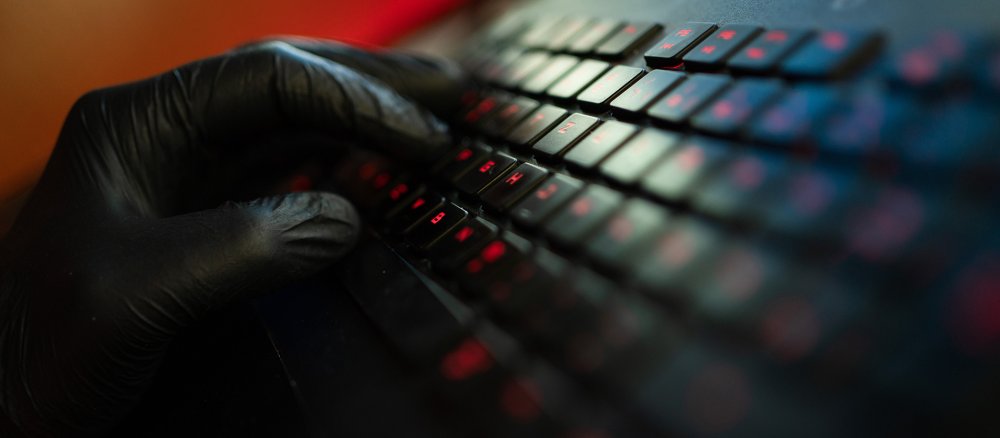 A hand in a black glove types on a keyboard in the semi-darkness