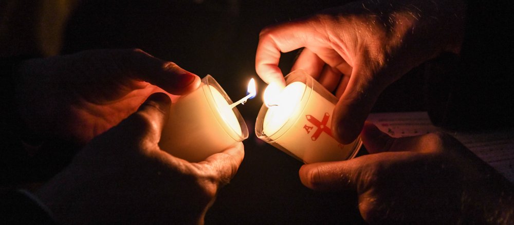 Ein Mensch gibt das Licht der Osterkerze an einen anderen Menschen weiter