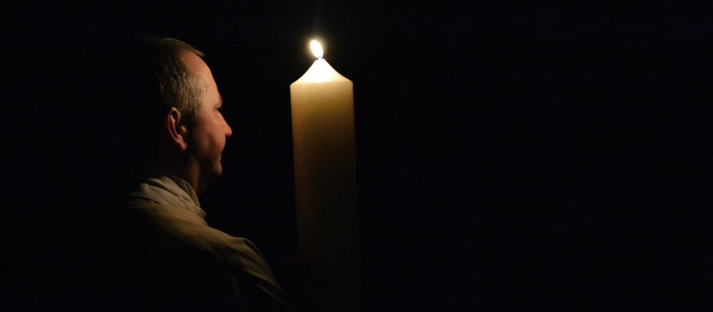 Ein Priester trägt die Osterkerze zum Beginn der Feier der Osternacht in die noch dunkle Kirche.