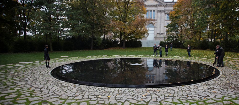 Interessierte stehen in Berlin an der Gedenkstätte für die im Nationalsozialismus ermordeten Sinti und Roma. Das Denkmal liegt im Tiergarten direkt neben dem Bundestag.
