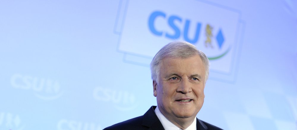 Horst Seehofer vor einem Plakat der CSU, lächelnd.